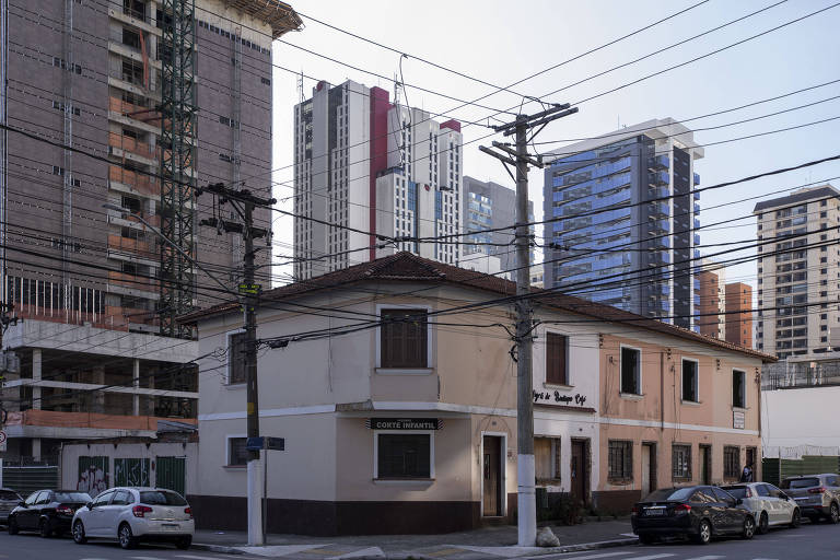 Imagem mostra esquina com cinco sobrados com cores terrosas ao lado de um grande prédio em construção e com outros ao fundo