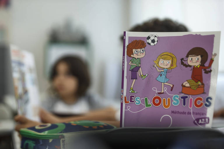 Foco na capa de livro didático de francês, que tem capa roxa e três crianças brincando com uma bola de futebol