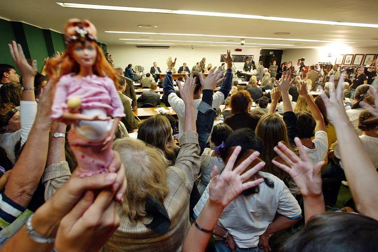 Manifestantes contra o aborto durante erguem as mãos no fundo de sala na Câmara dos Deputados; à esquerda, há uma boneca grávida