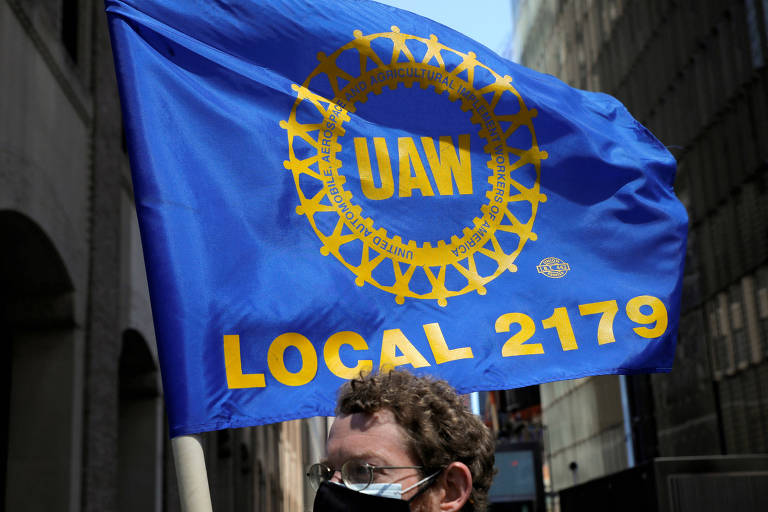 Trabalhador segura bandeira azul com as letras UAW em amarelo
