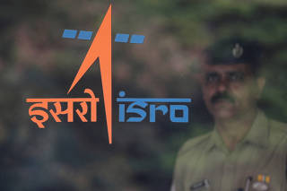 FILE PHOTO: A security guard stands behind the logo of Indian Space Research Organisation (ISRO) at its headquarters in Bengaluru