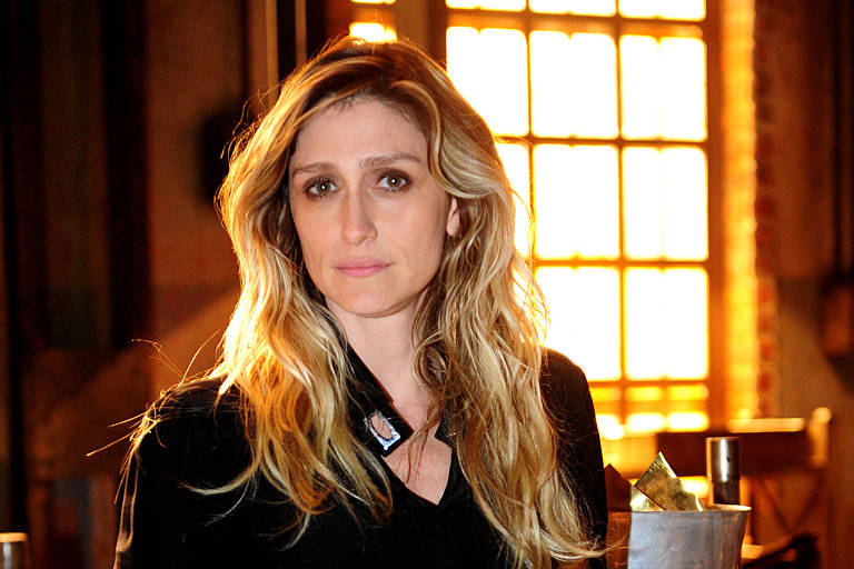 Em foto colorida, mulher vestida toda de preto posa em um cenário de novela