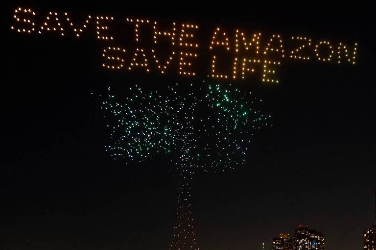 Drones formam uma árvore de cor verde, com os dizeres "salve a Amazônia, salve a vida" em amarelo, no céu de Manhattan, Nova York, próximo a uma movimentada avenida