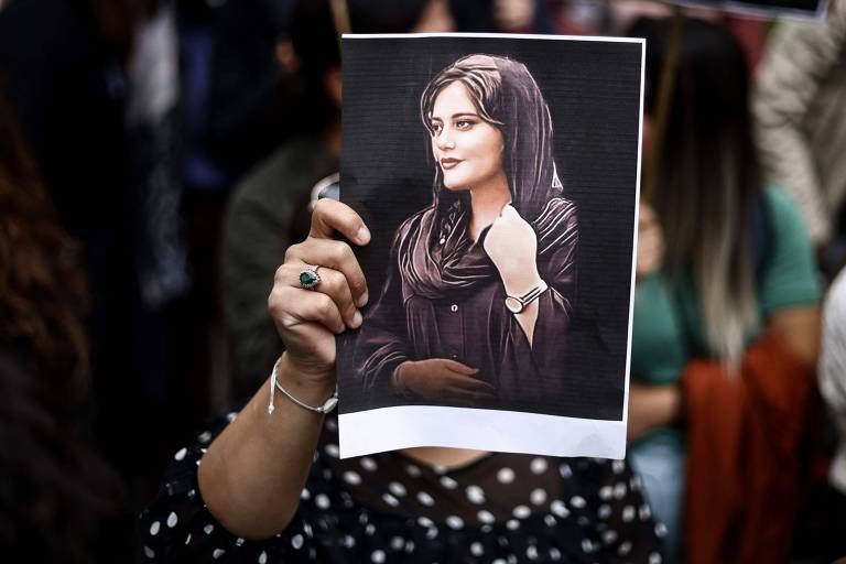 Manifestante segura cartaz com ilustração do rosto de Mahsa Amini durante ato em apoio aos protestos de iranianos na embaixada do país em Bruxelas 