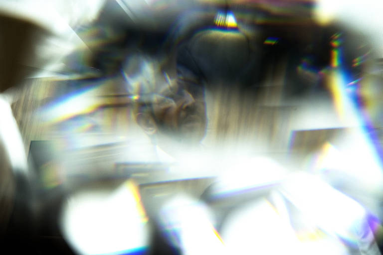 Prefeito Ricardo Nunes visto através de reflexos de vidro na mesa de seu gabinete