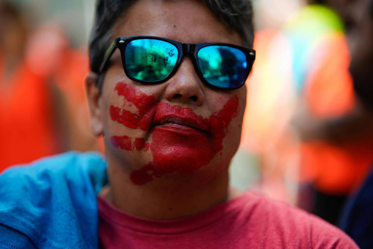 Homem branco com o rosto pintado, uma mão vermelha na região de sua boca, como se alguém quisesse cobrí-la, durante protesto no início da Semana do Clima em Nova York