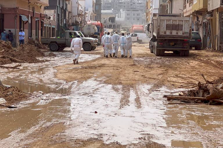 Homens vestidos com roupas brancas caminham em rua coberta de lama