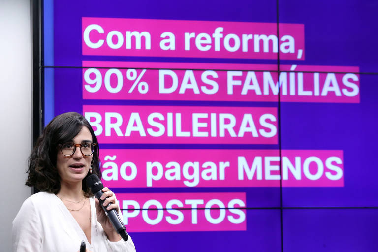 Mulher de óculos com microfone diante de painel com a frase "com a reforma, 90% das famílias brasileiras vão pagar menos impostos