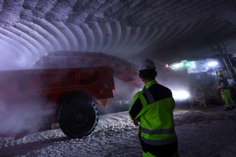 Homem com capacete branco e jaleco verde observa máquina realizando escavação em mina na Alemanha