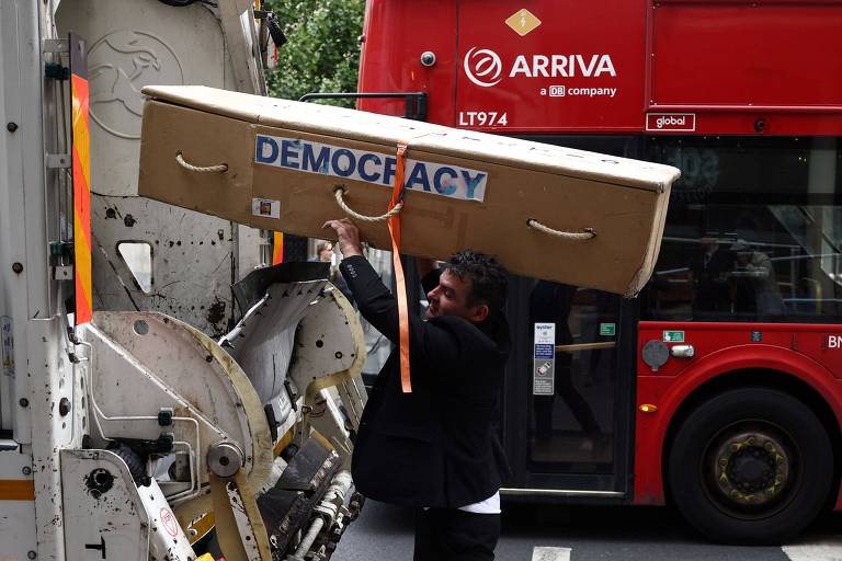 Manifestante joga em caminhão de lixo caixão com a palavra 'democracia' durante protesto em Londres, no Reino Unido, contra a expansão de uma área de baixas emissões por veículos