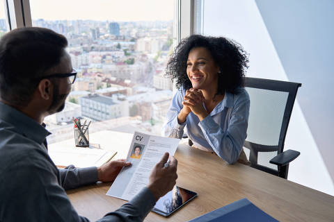 Friendly interview between Indian businessman hr director holding paper cv hiring for job female African American applicant manager sitting in contemporary office. Human resources recruitment concept Credit Insta Photos / AdobeStock