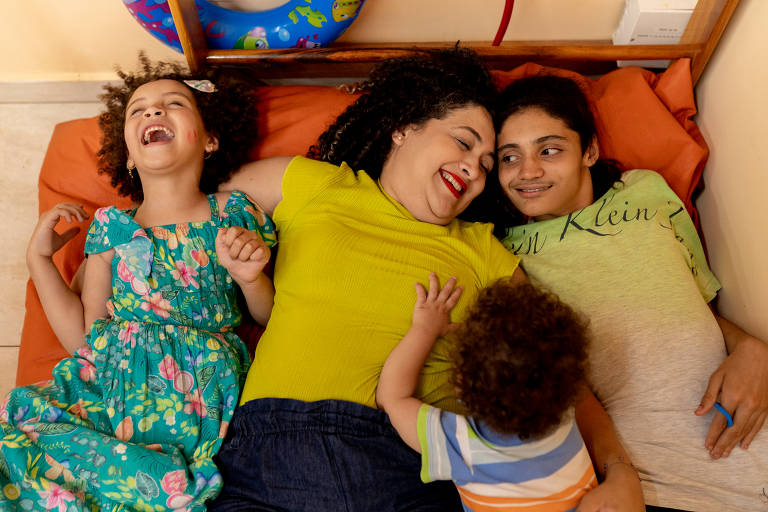 Ariene Pereira Menezes (camisa verde musgo) e seus três filhos: Chryslander (camisa verde claro), Khyara (vestidinho) e Benício (camisa polo litrada); ela está deitada entre eles os abraçando