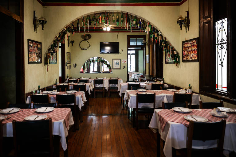 Imagem do salão principal de uma cantina italiana, com mesas dispostas lado a lado e quadros nas paredes