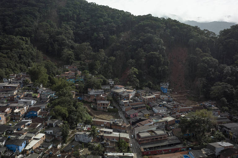 Vista aérea mostra casas próximas ao morro, onde ainda é possível ver clareiras abertas na mata pelos deslizamentos