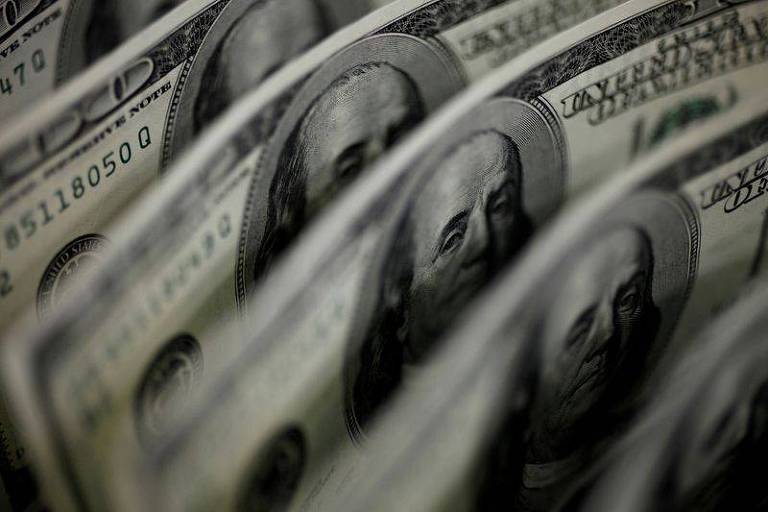 A imagem mostra uma série de notas de cem dólares americanos alinhadas em uma perspectiva que cria um efeito de repetição. O foco seletivo destaca a figura de Benjamin Franklin, que aparece na nota, e a textura do papel-moeda.