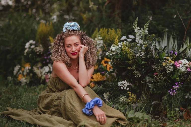 Chloe Homan é fotografada com mão esquerda apoiada no braço direito e cercada por flores