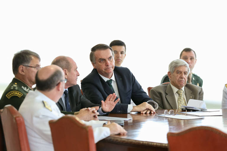 Bolsonaro e Heleno estão sentados à mesa ao lado do ex-ministro Fernando Azevedo e dos comandantes das Forças Armadas