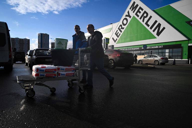 Imagem mostra duas pessoas andando enquanto empurram um carrinho de comprar em frente à uma unidade da Leroy Merlin