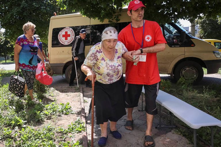 Voluntário da Cruz Vermelha ajuda uma senhora durante a evacuação da cidade de Kupiansk-Vuzlovyi, na Ucrânia, durante um dos ataques da Rússia