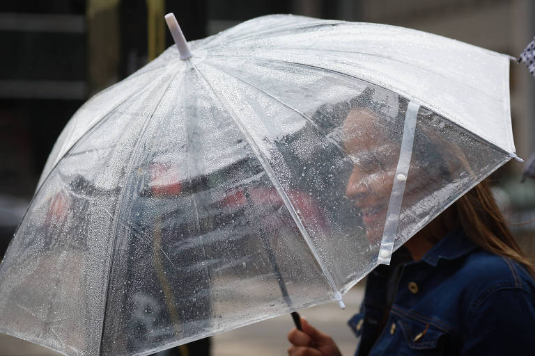 Mulher se protege da chuva com uma sombrinha de material transparente