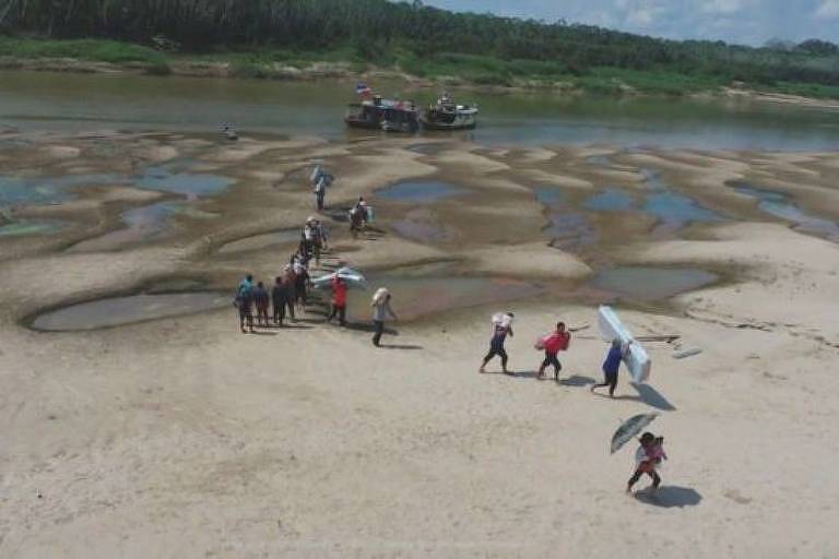 Pessoas caminham em areia em leite seco de rio