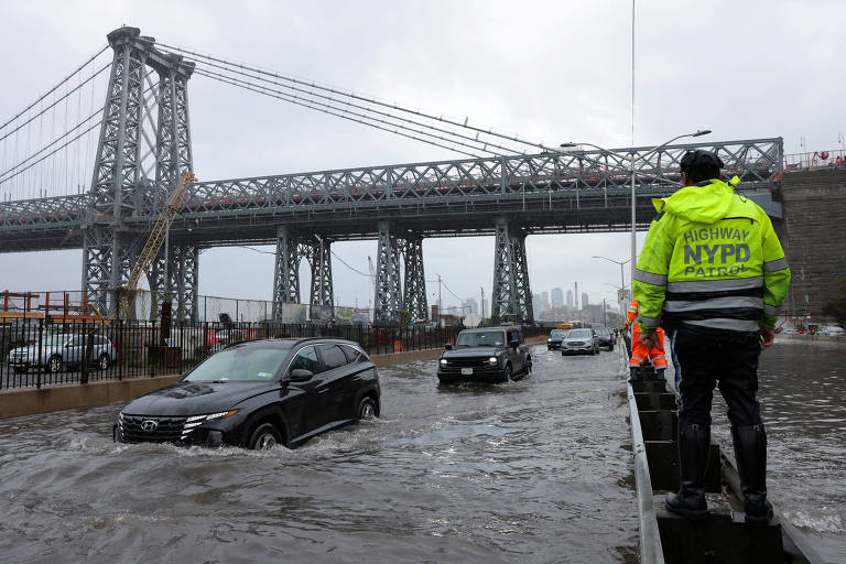 Policial em rua alagada após tempestade em Manhattan, próximo à ponte Williamsburg, em Nova York