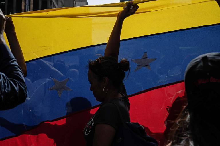 Mulher de mão erguida diante de bandeira amarela, azul e vermelha