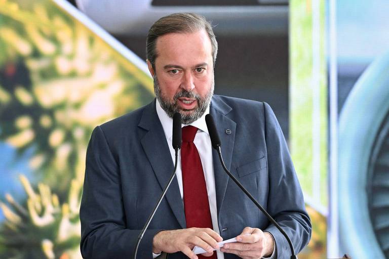 Silveira é um homem grisalho, de barba. Veste costume azul, camisa branca e gravata vermelha.