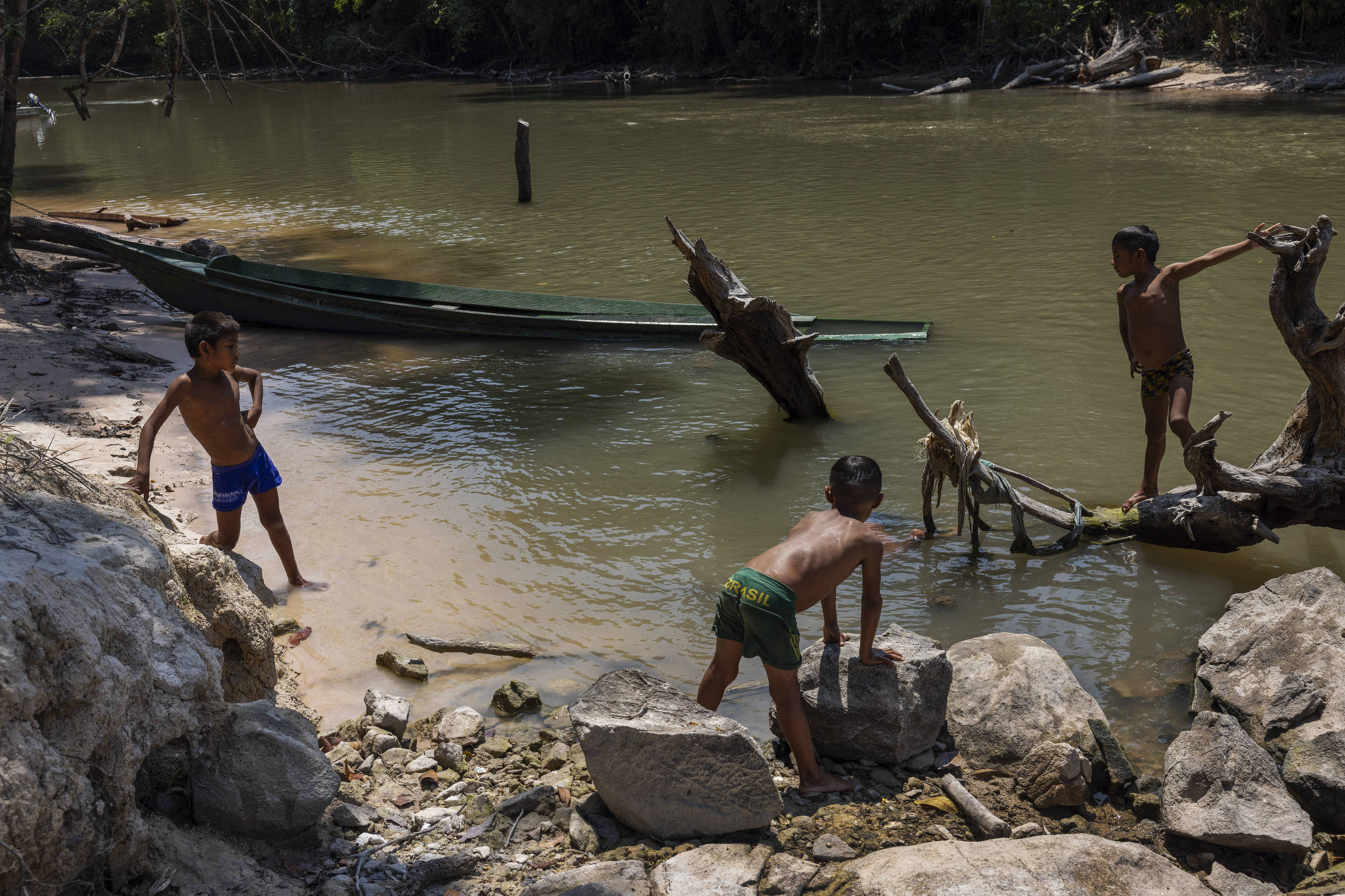 Três meninos na beira do rio com uma canoa atracada perto do grupo