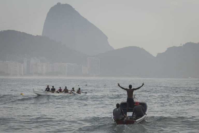 Pescadores da colônia Z-13 entram de barco no mar de Copacabana com o Pão de Açúcar ao fundo; um dos homens reza