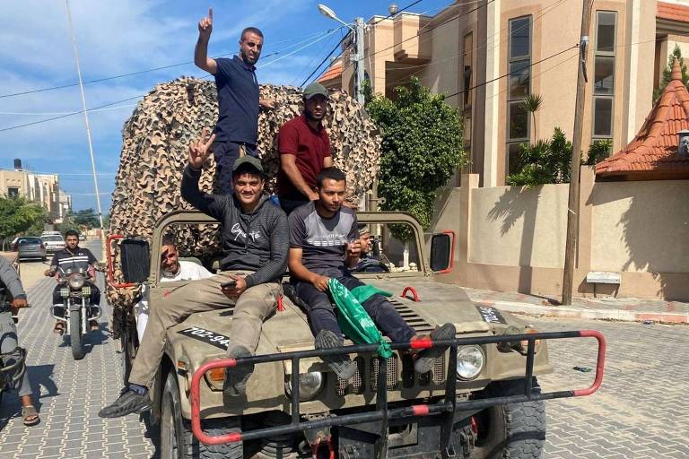 Palestinos comemoram enquanto viajam em um veículo militar israelense que foi apreendido por homens armados que invadiram áreas do sul de Israel