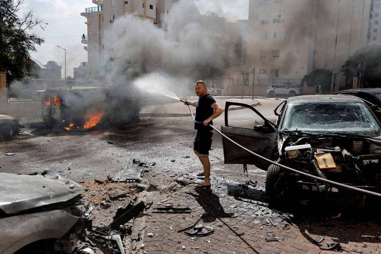 Um homem tenta apagar um incêndio numa van, enquanto foguetes são lançados da Faixa de Gaza, em Ashkelon, sul de Israel