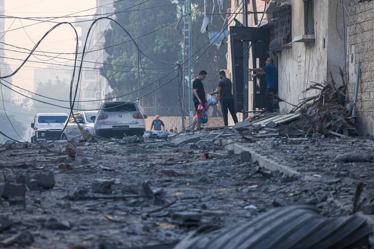 Pessoas caminham por ruínas em rua afetada por ataques aéreos israelenses