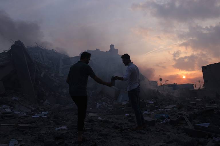 Homens palestinos procuram objetos pessoais em frente às ruínas de prédio destruído em Gaza