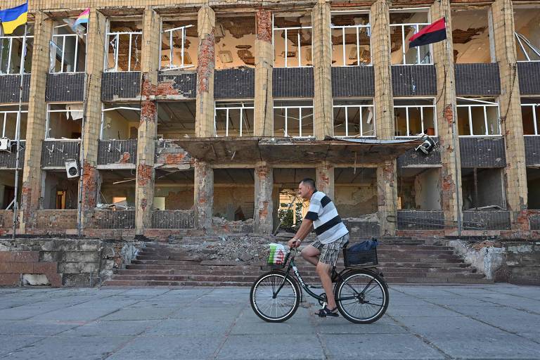 Um morador local passa de bicicleta por um prédio destruído na cidade de Kupiansk, região de Kharkiv
