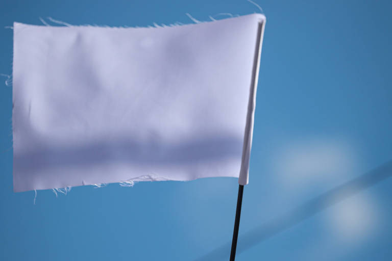 Uma mão para o alto segurando uma bandeira totalmente branca sob um céu azul com poucas nuvens