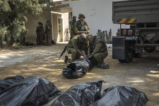 Israeli soldiers check the bodies of people killed in Kfar Azza, a village just across the border from Gaza that was attacked by Palestinian gunmen, in Israel, Tuesday, Oct. 10, 2023. (Sergey Ponomarev/The New York Times)