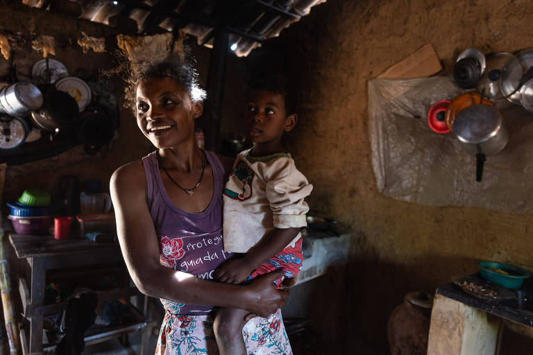 De pé, a dona de casa Marizete dos Santos e seu filho Davi, que está em seu colo, não têm cisterna em casa e dependem de caminhão-pipa em Betânia do Piauí (PI).