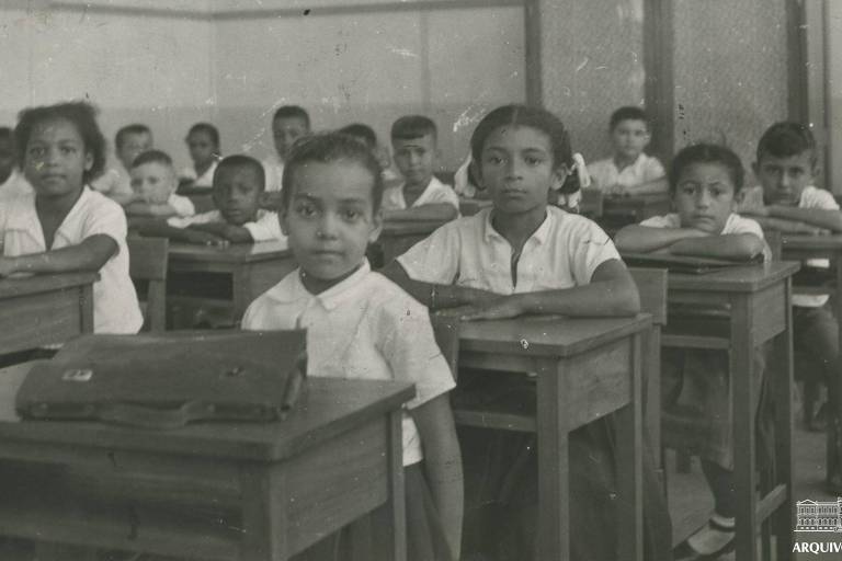 Crianças em escola no Rio, sentadas em suas cadeiras, olham para câmera