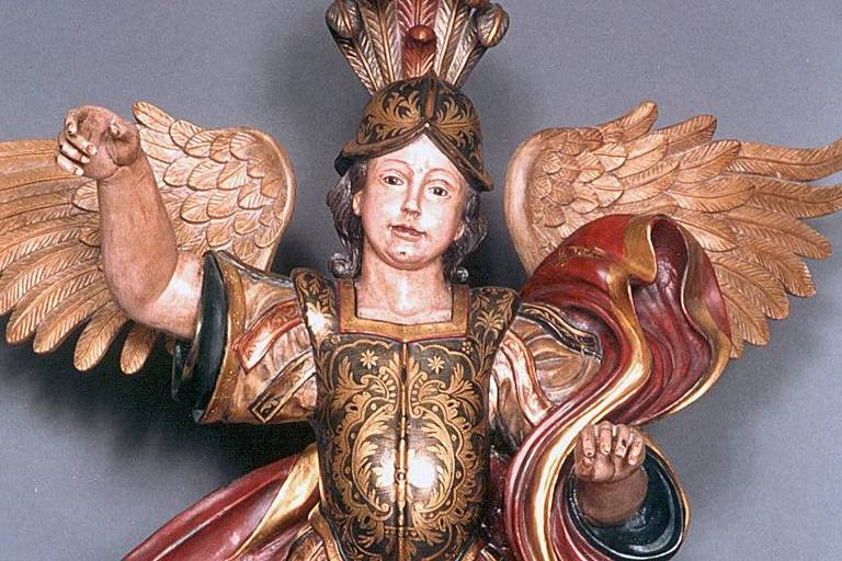 A escultura é colorida, feita em estilo barroco, e mostra o arcanjo vestindo uma armadura, capacete e exibindo suas asas