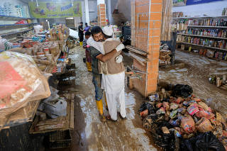 Two men embrace inside a damaged grocery store affected by fatal floods, in Derna