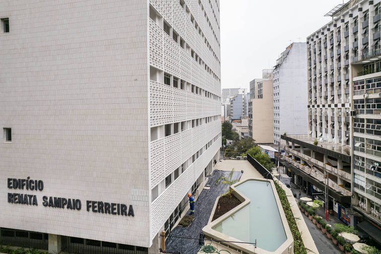 Imagem do alto mostra a piscina com bordas que forma um polígono diante da fachada de tijolos vazados do prédio. Na lateral é possível ler Edífcio Renata Sampaio Ferreira 