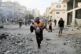 Palestinian man carries a wounded girl at the site of Israeli strikes in Khan Younis