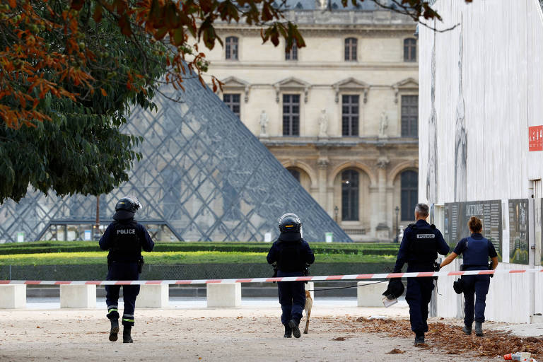 Policiais caminham no pátio do museu com a famosa pirâmide de vidro ao fundo