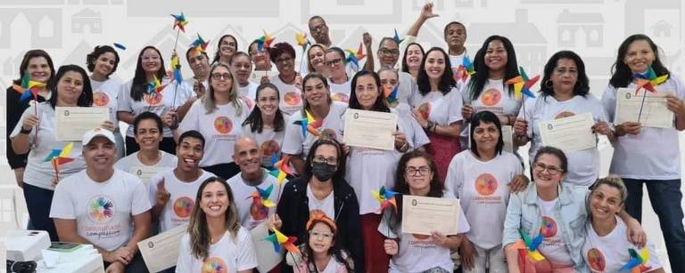 Grupo de diversas mulheres e alguns homens vestindo camisa do Projeto Favela Compassiva: Rocinha e Vidigal. Alguns mostram seus certificados de capacitação