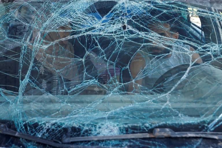 Casal espera para abastecer em posto de gasolina dentro de carro que foi danificado pelos ataques israelenses