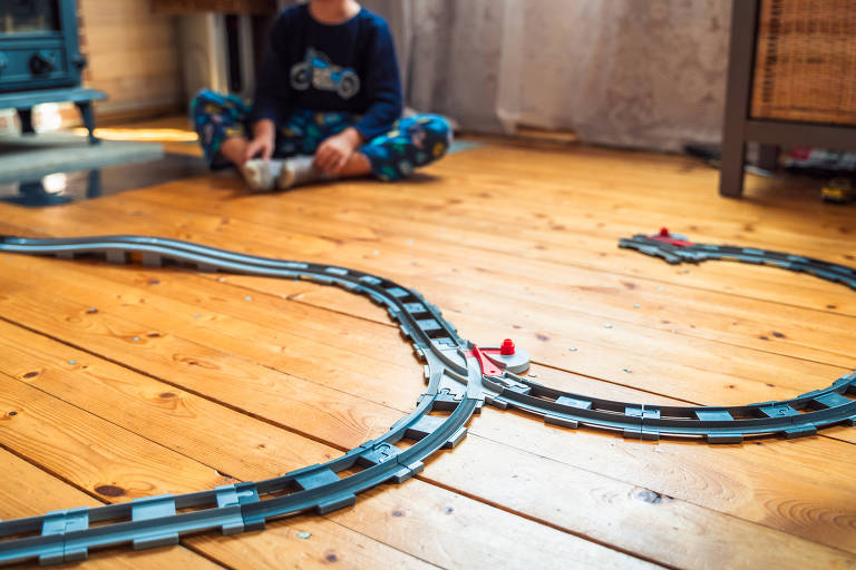 Tremzinho incompleto de brinquedo; ao fundo, uma criança com as pernas cruzadas