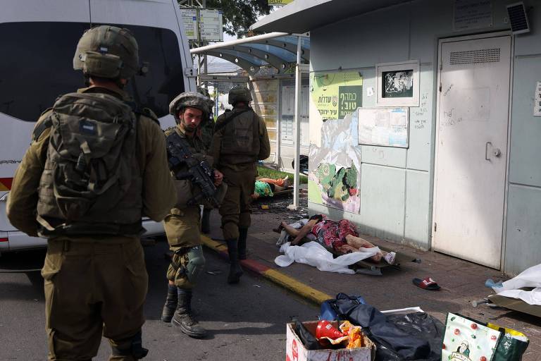 Soldados israelenses próximos aos corpos de civis na rua da cidade de Sderot, próxima à Faixa de Gaza, no sábado (7), quando terroristas do Hamas atacaram Israel