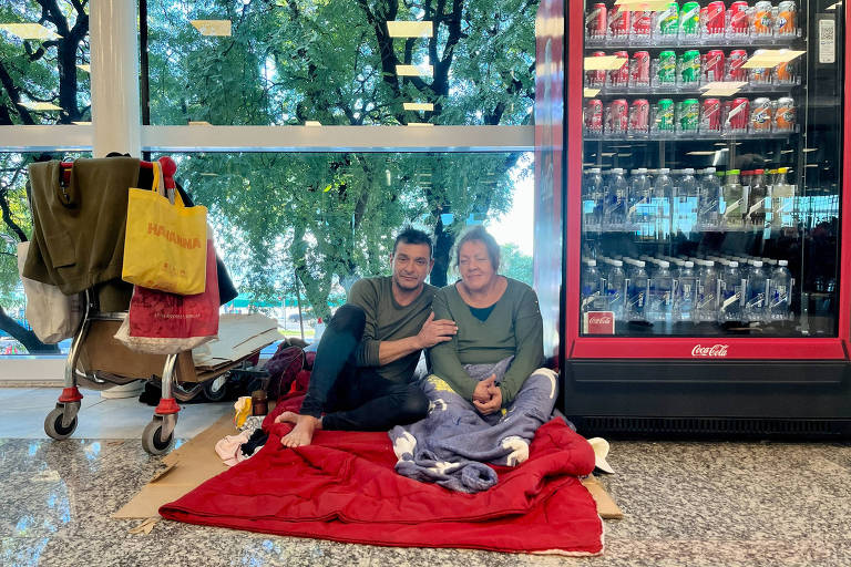 casal sentado no chão sobre uma manta vermelha, ao lado de uma vending machine