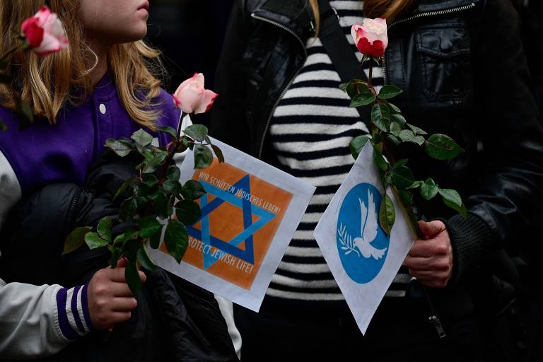 A imagem mostra duas pequenas bandeiras (estrela de Davi e pombo carregando ramo) em apoio a Israel nas mãos de duas pessoas; não é possível ver o rosto delas 